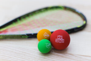 Image de trois balle de squash avec le texte "mini squash" écrit dessus, et une raquette en arrière plan.